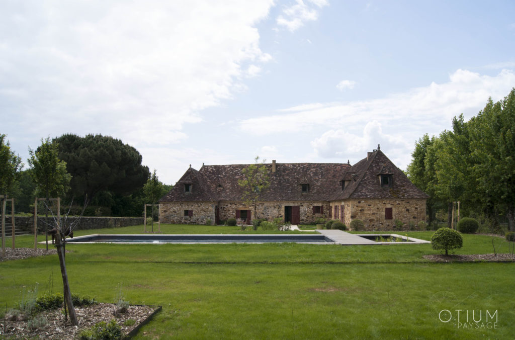 Jardin situé à Molières avec une piscine en premier plan et une ferme du Périgord. Ce jardin a été aménagé par l'agence otium paysage